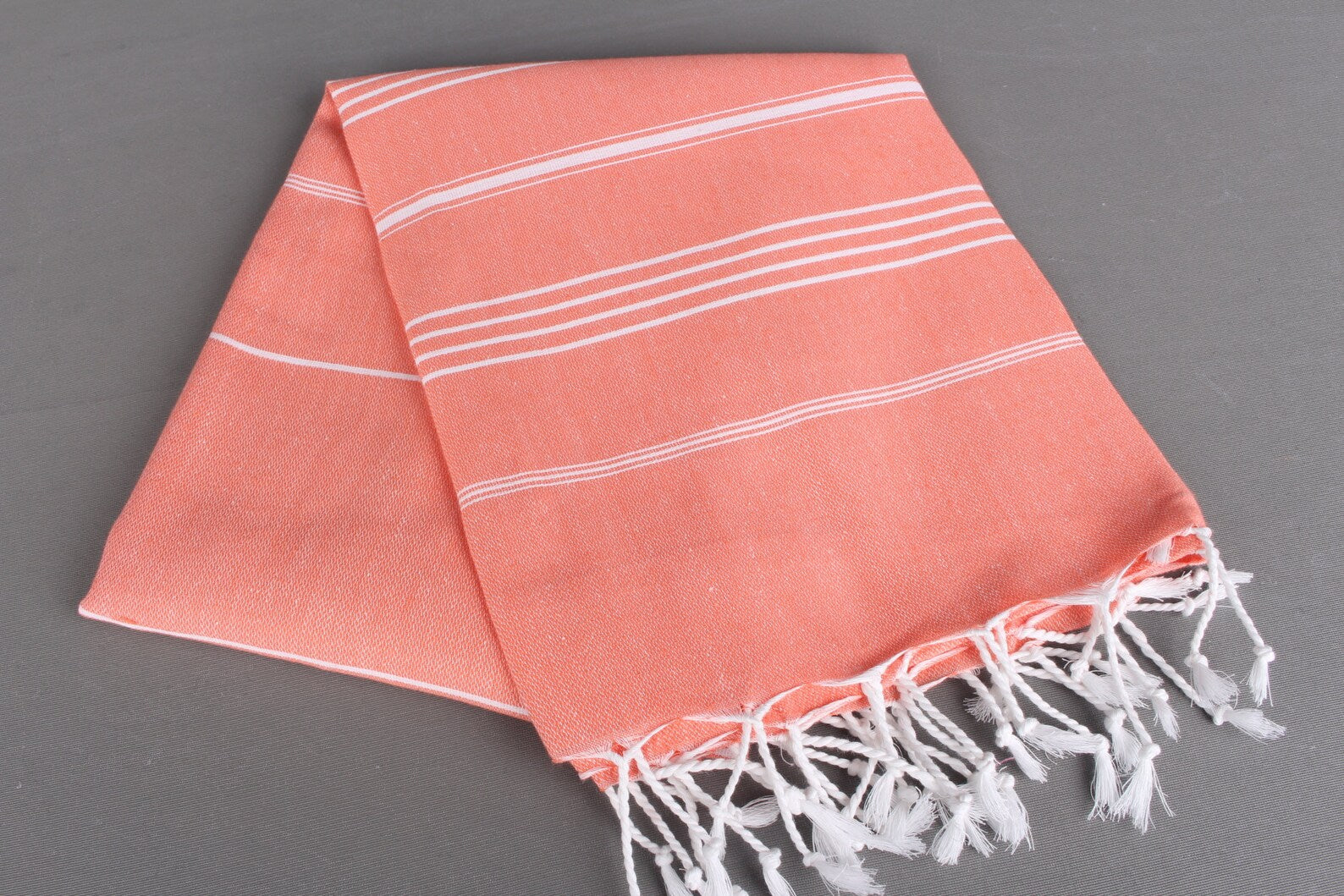 Coral lightweight hamam towel with white stripes and fringes on a gray background