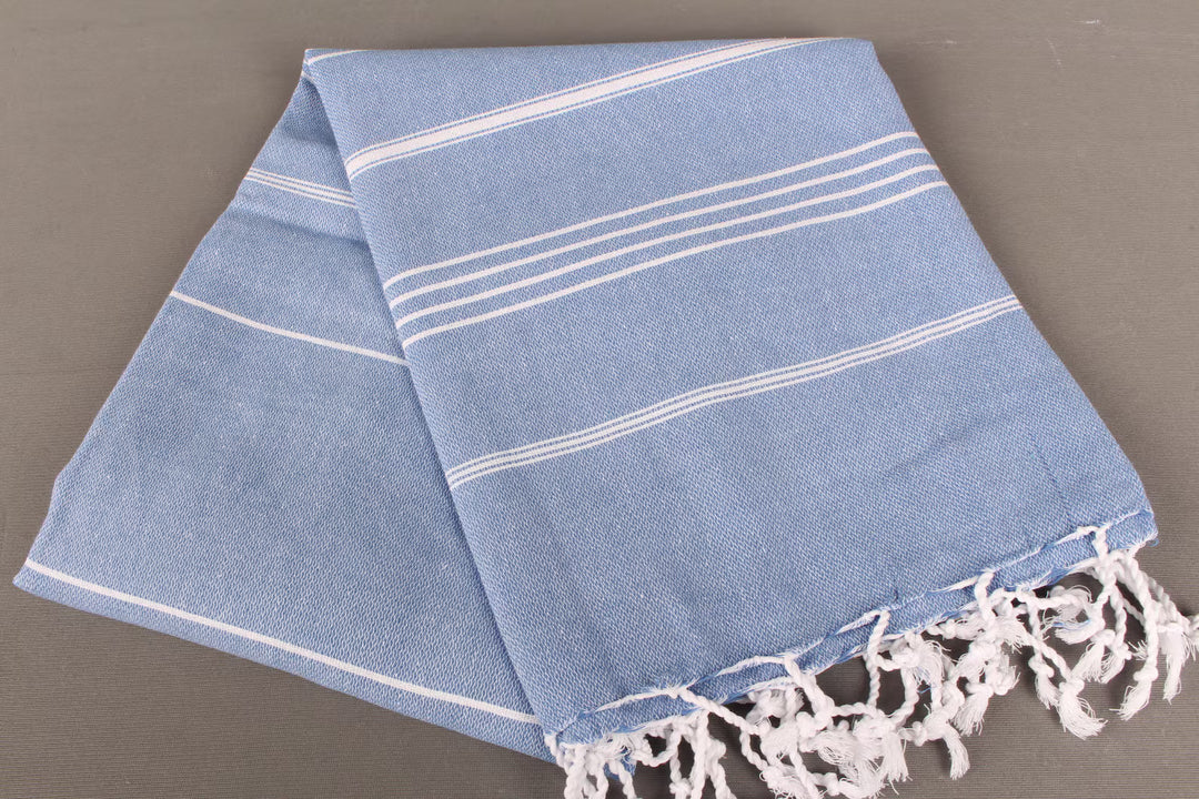 Blue towel light weight with white stripes and fringes on a gray background
