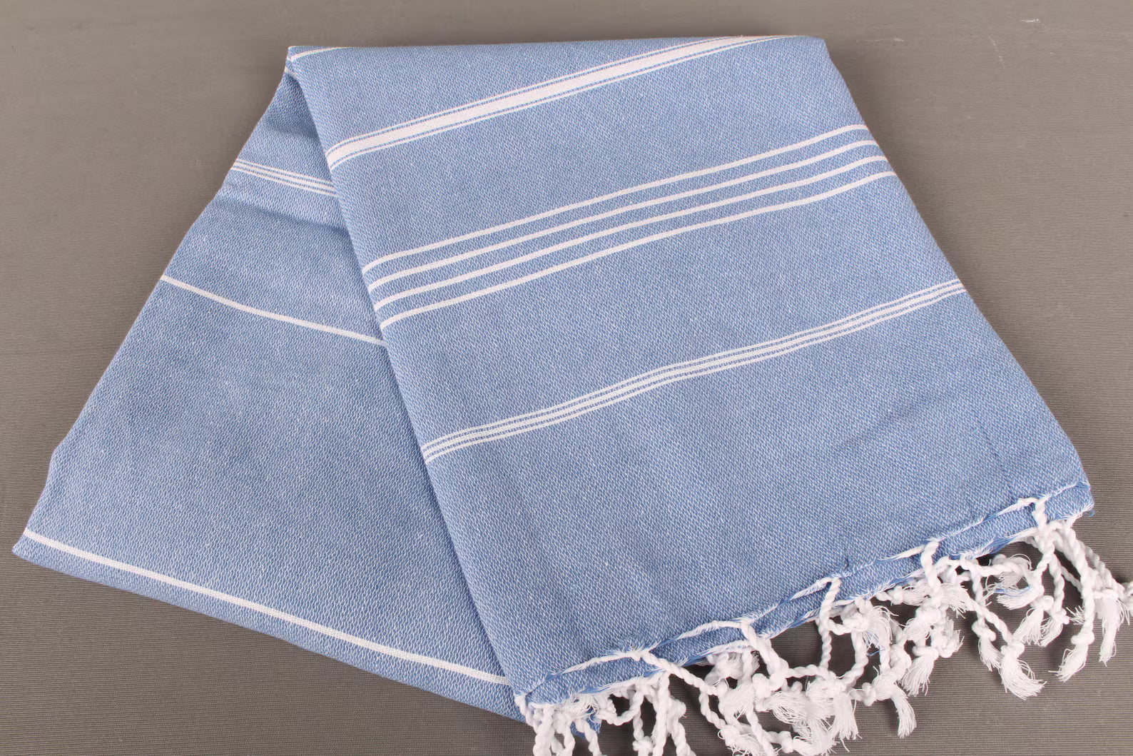 Blue towel light weight with white stripes and fringes on a gray background