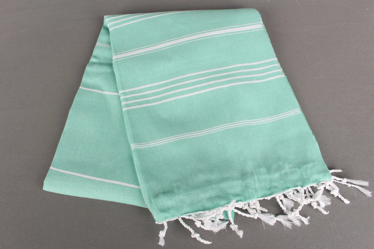 Turquoise lightweight hamam towel with white stripes and fringes on a gray background