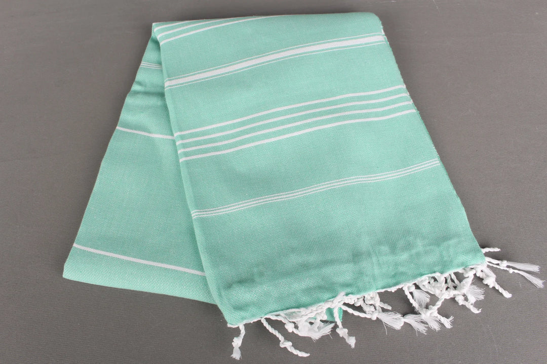 Turquoise lightweight hamam towel with white stripes and fringes on a gray background