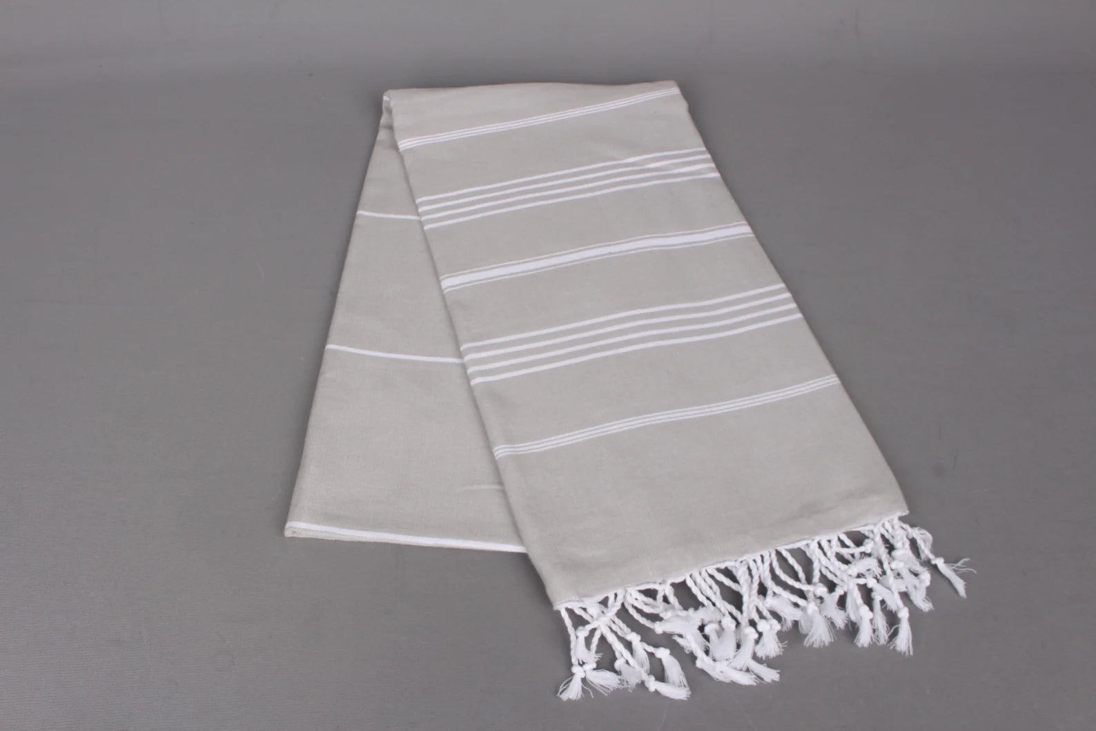 Gray  lightweight hamam towel with white stripes and fringes on a gray background