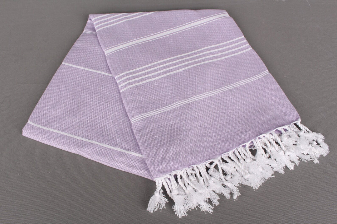 Lavender lightweight hamam towel with white stripes and fringes on a gray background