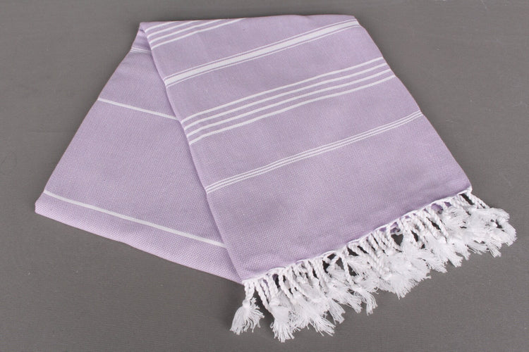 Lavender lightweight hamam towel with white stripes and fringes on a gray background