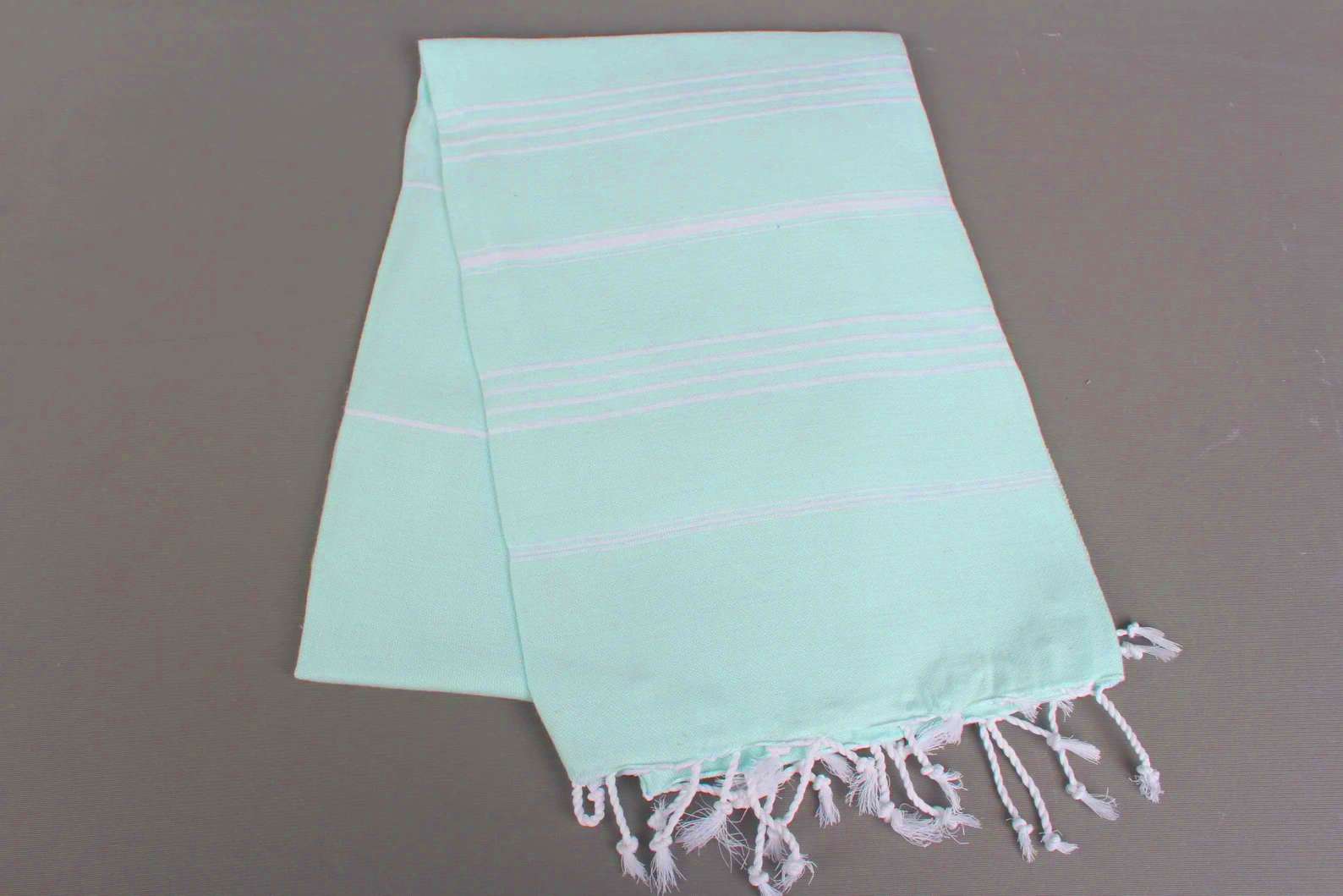 Mint lightweight hamam towel with white stripes and fringes on a gray background