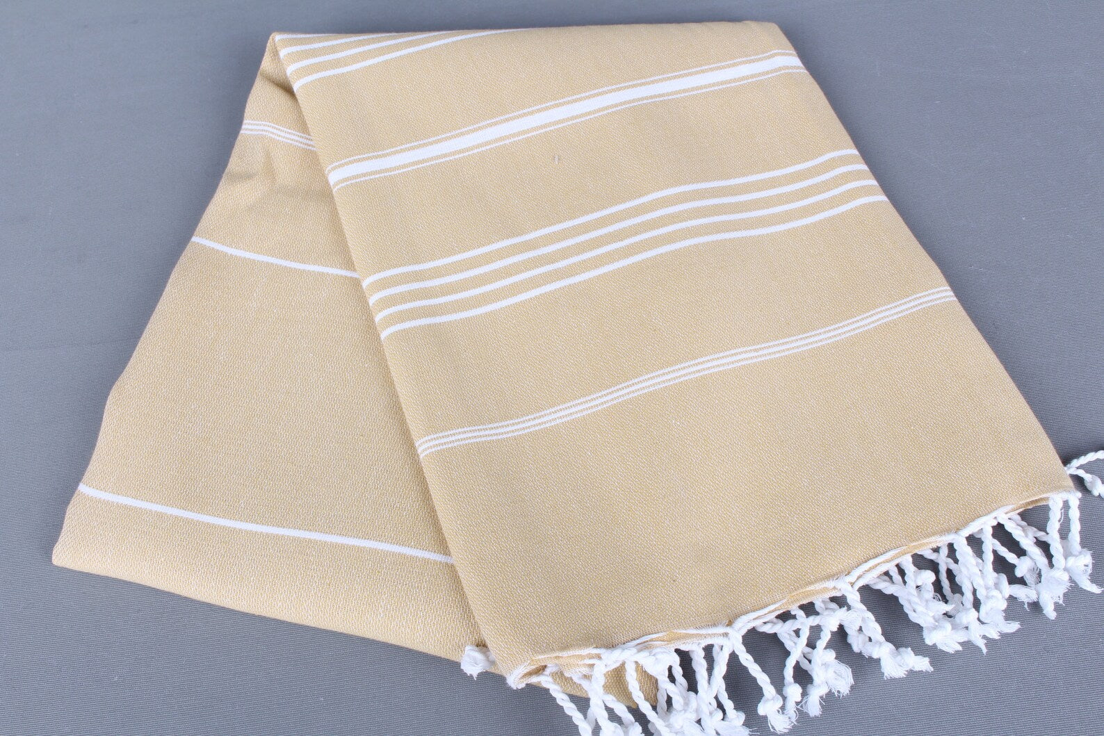 Beige lightweight hamam towel with white stripes and fringes on a gray background