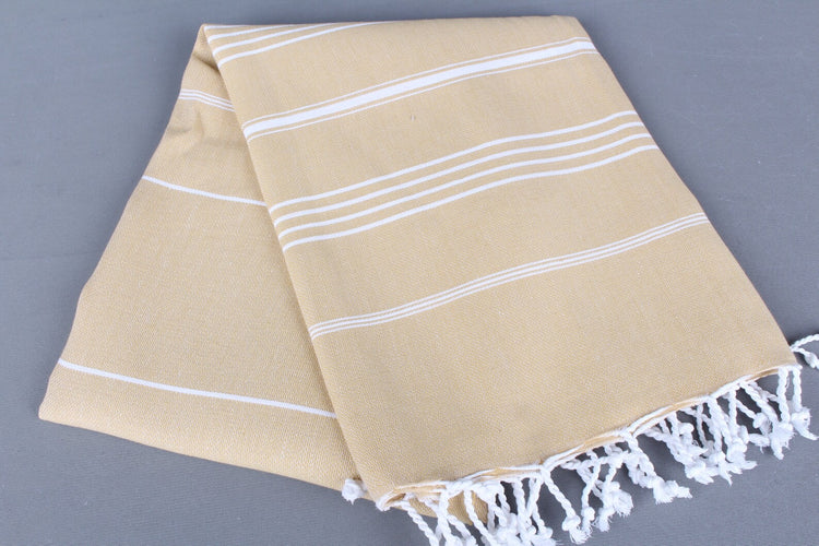 Beige lightweight hamam towel with white stripes and fringes on a gray background