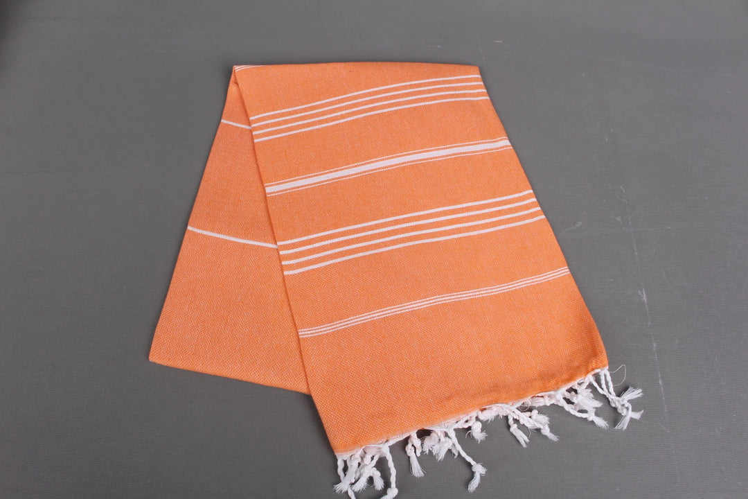 Orange lightweight hamam towel with white stripes and fringes on a gray background