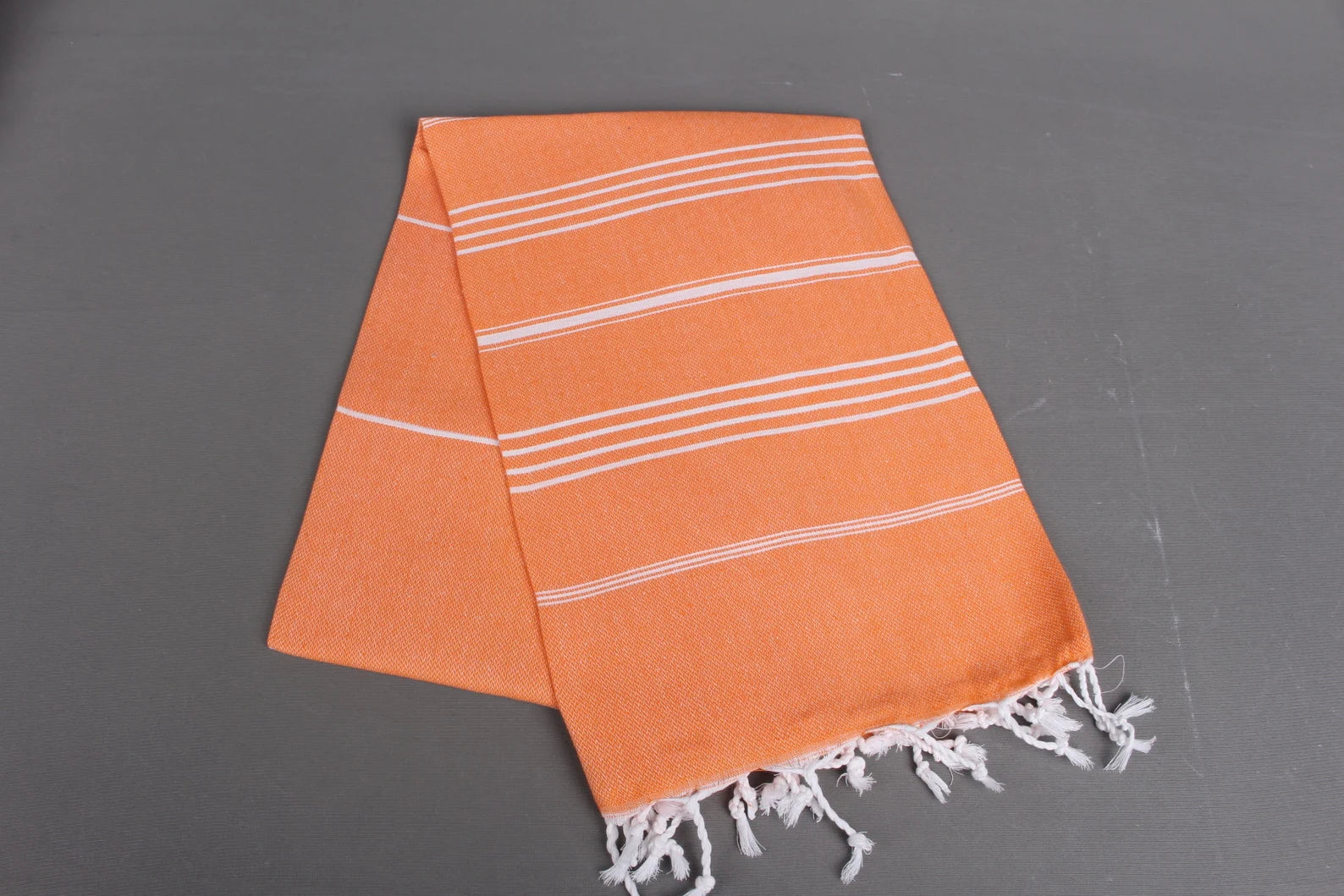 Orange lightweight hamam towel with white stripes and fringes on a gray background