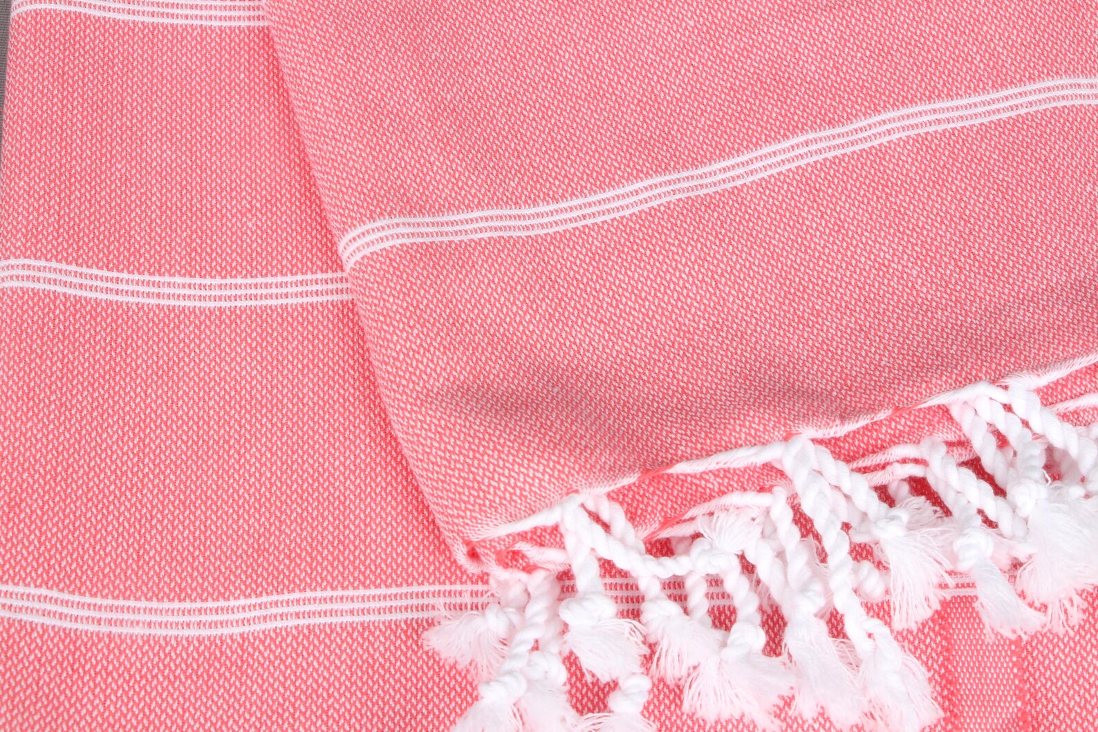 Close-up of a pink lightweight hamam  towel with white stripes and fringes