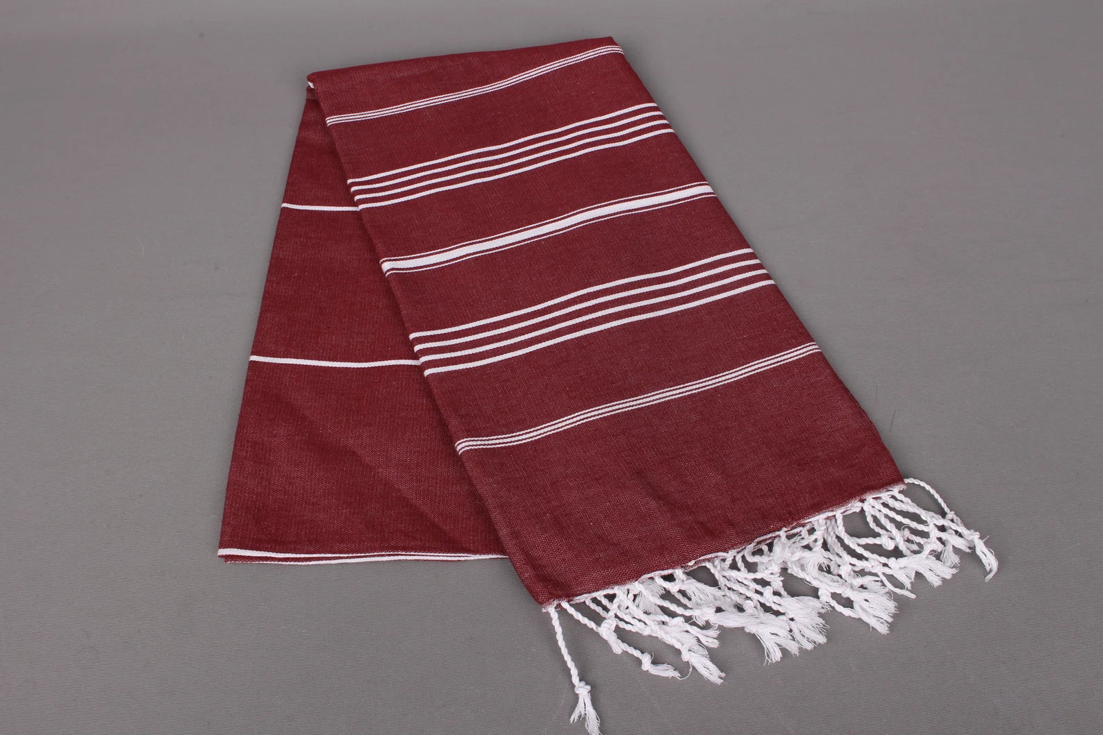 Red lightweight hamam towel with white stripes and fringes on a grey background