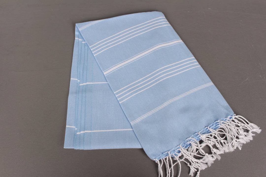 Light blue lightweight hamam  towel with white stripes and fringes on a gray background