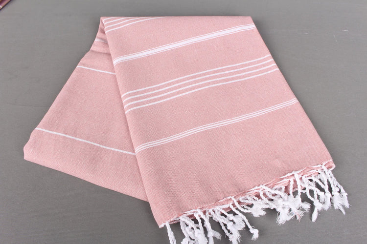 Pink lightweight hamam towel with white stripes and fringes on a gray background
