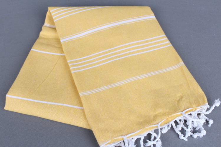Yellow lightweight hamam towel with white stripes and fringes on a gray background
