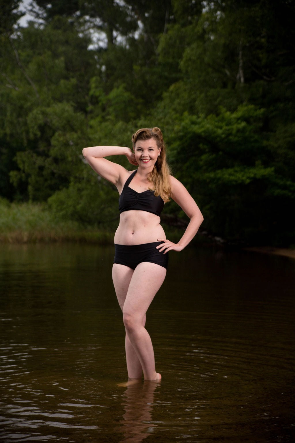 Woman in a black bikini standing in water with trees in the background