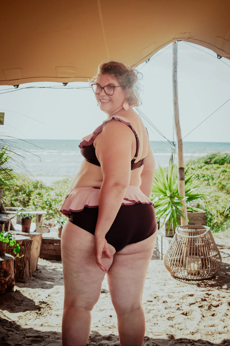 Woman in a bikini standing under a tent with a beach and palm trees in the background
