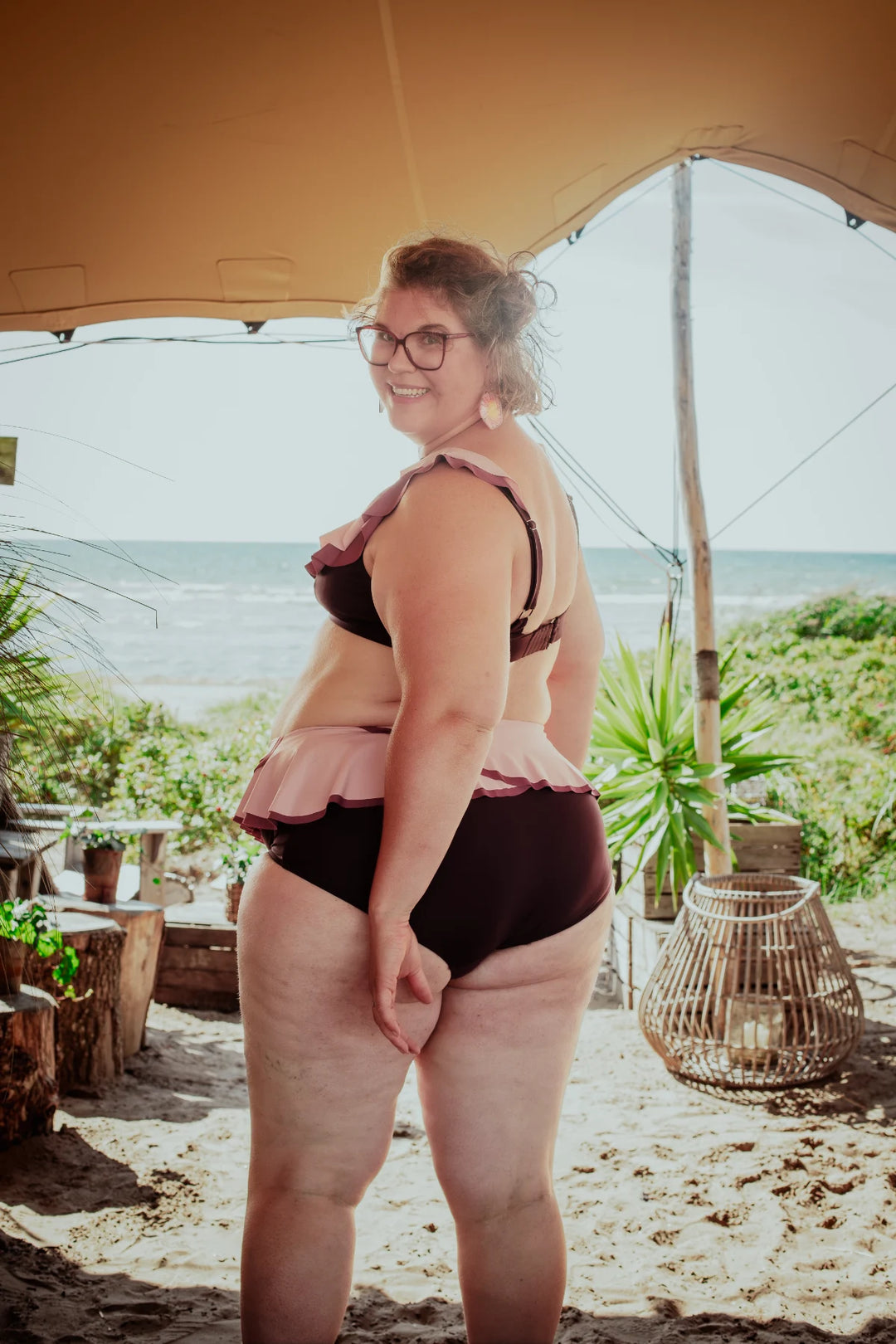 Woman in a bikini standing under a tent with a beach and palm trees in the background