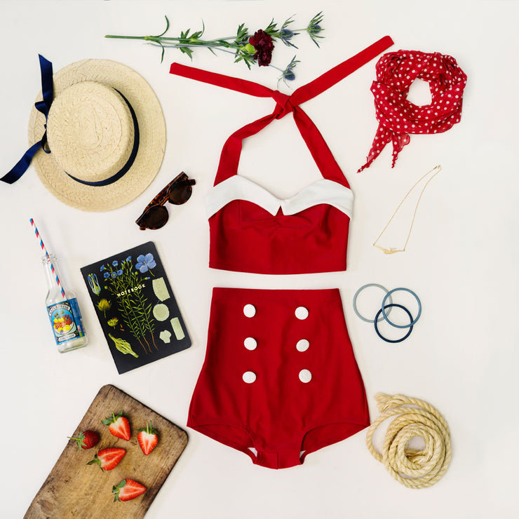 Flatlay of Red Hello sailor bikini with flower, strawberries, Sunhat, sunglasses, matching red scarf and more summer items.